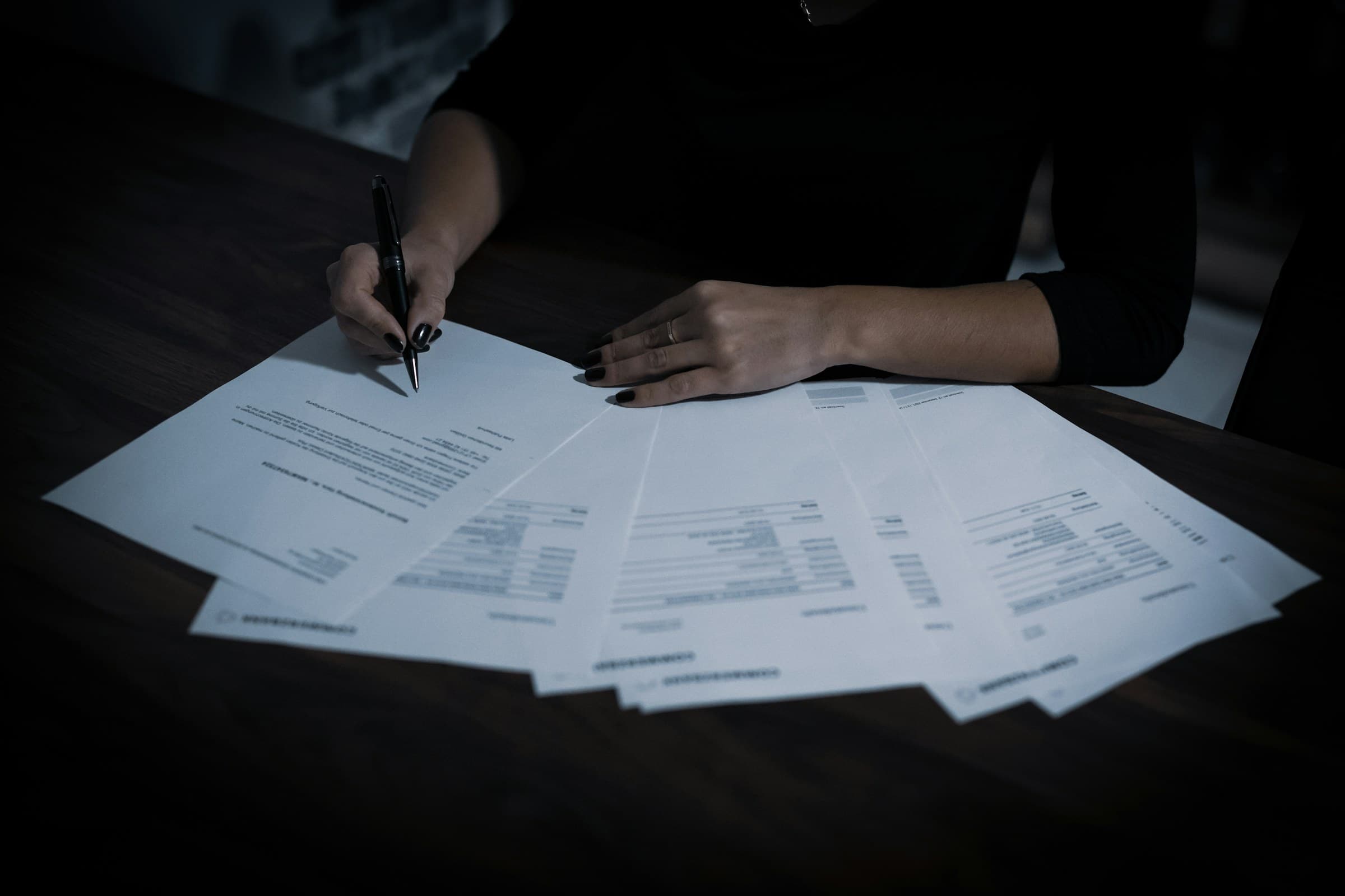 A person signing documents at a dark desk