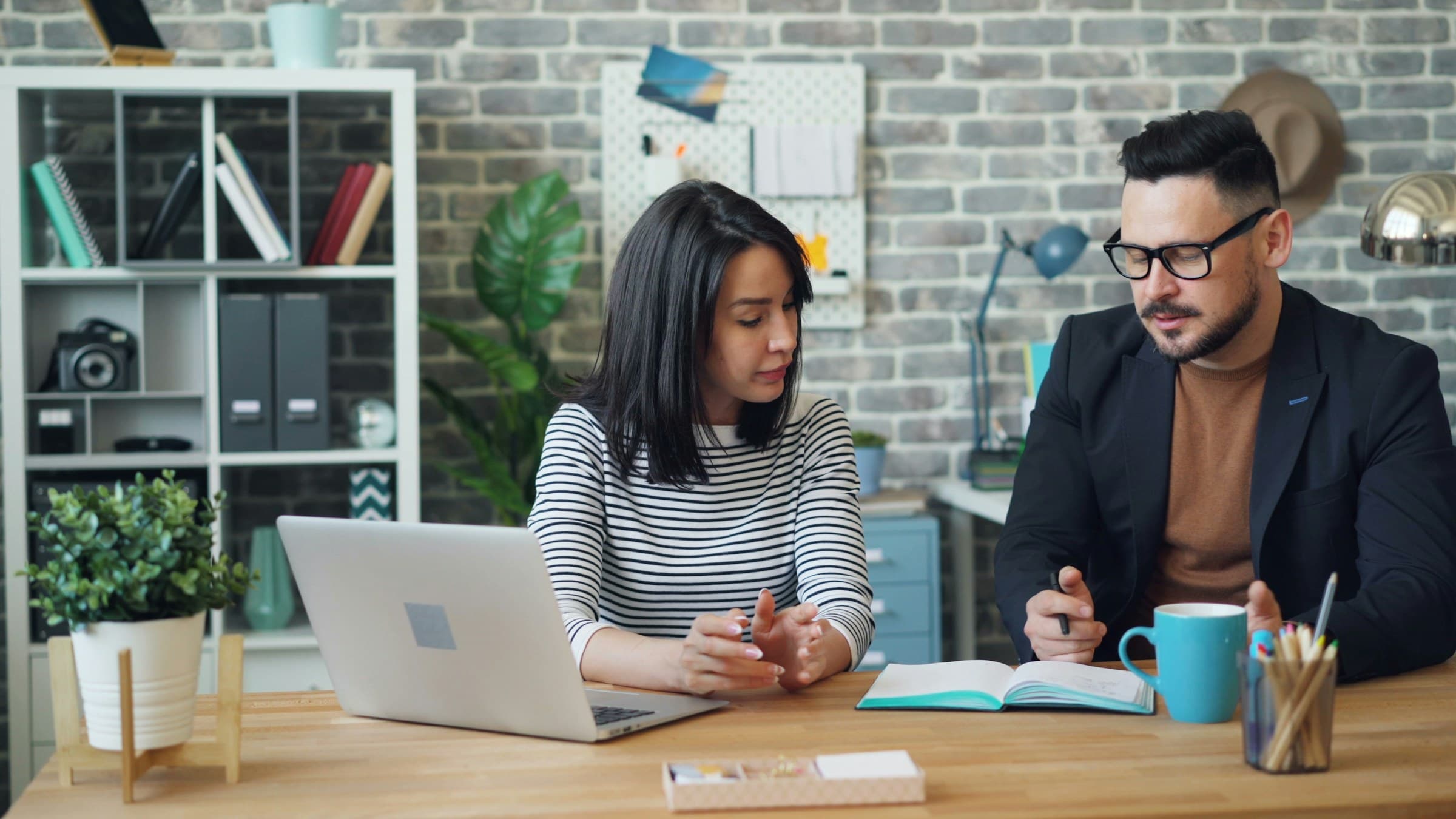 Two colleagues at a table beside a brick wall