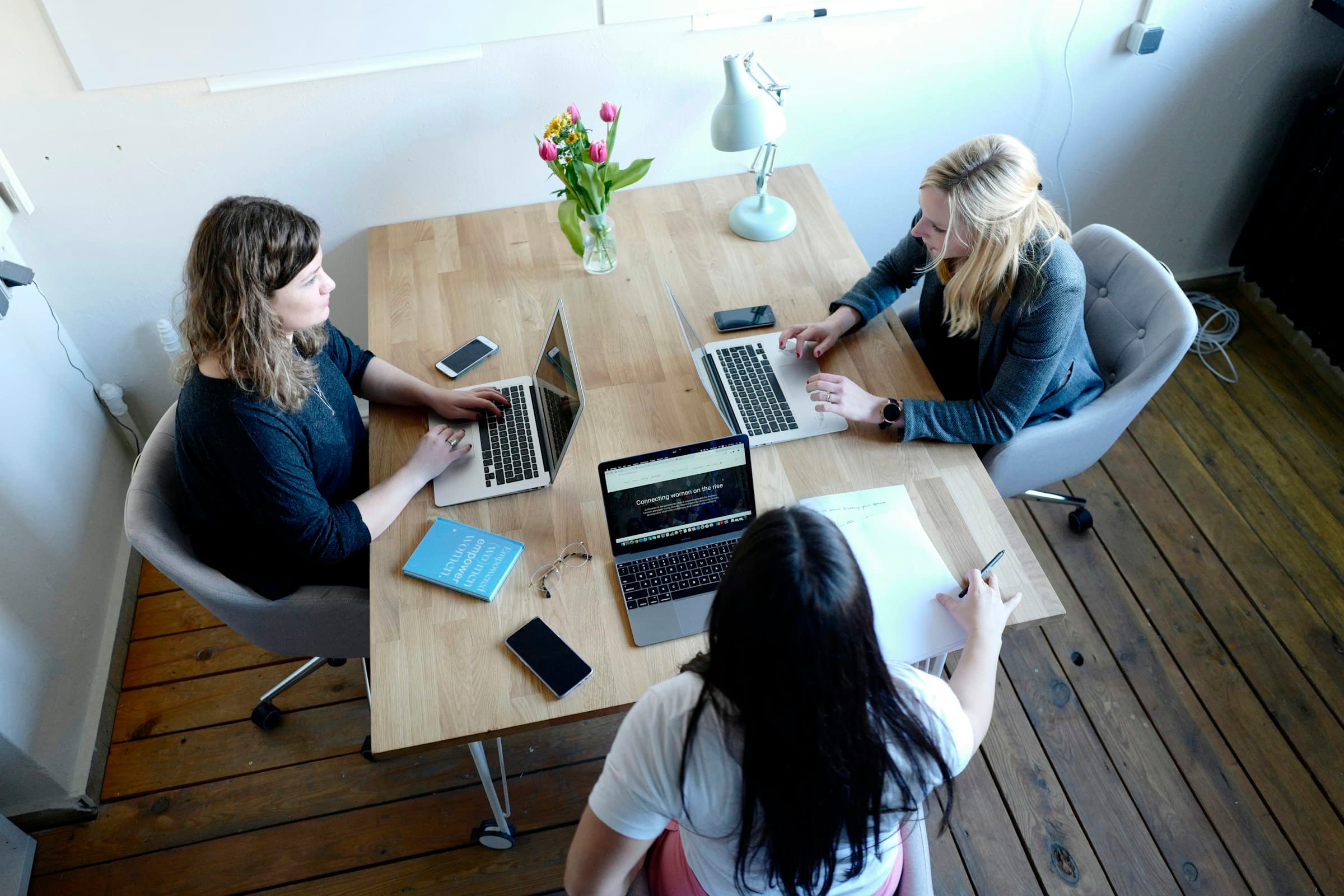 Three people with laptops at a wooden table seen from above