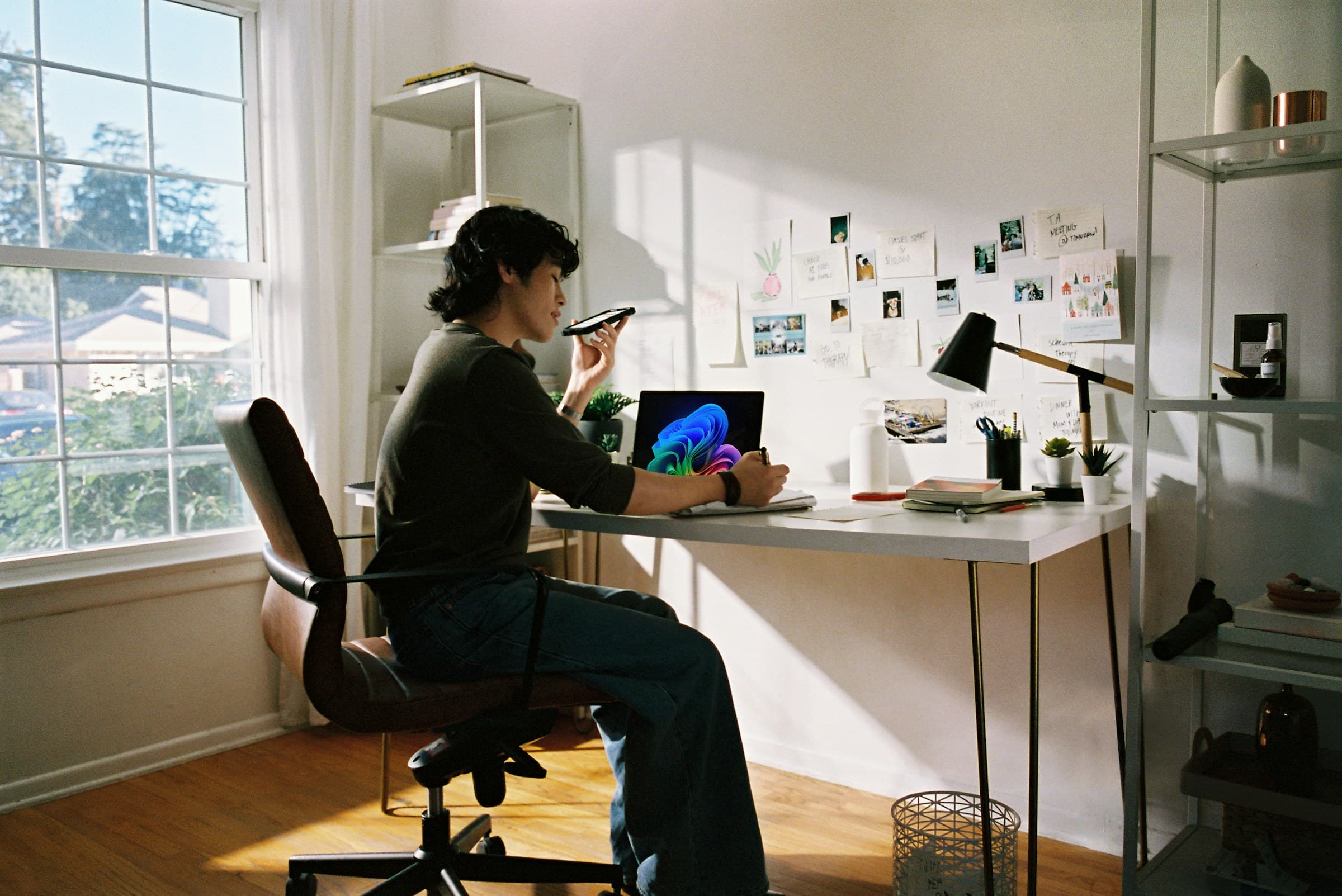 A person at a desk by a sunny window taking a call