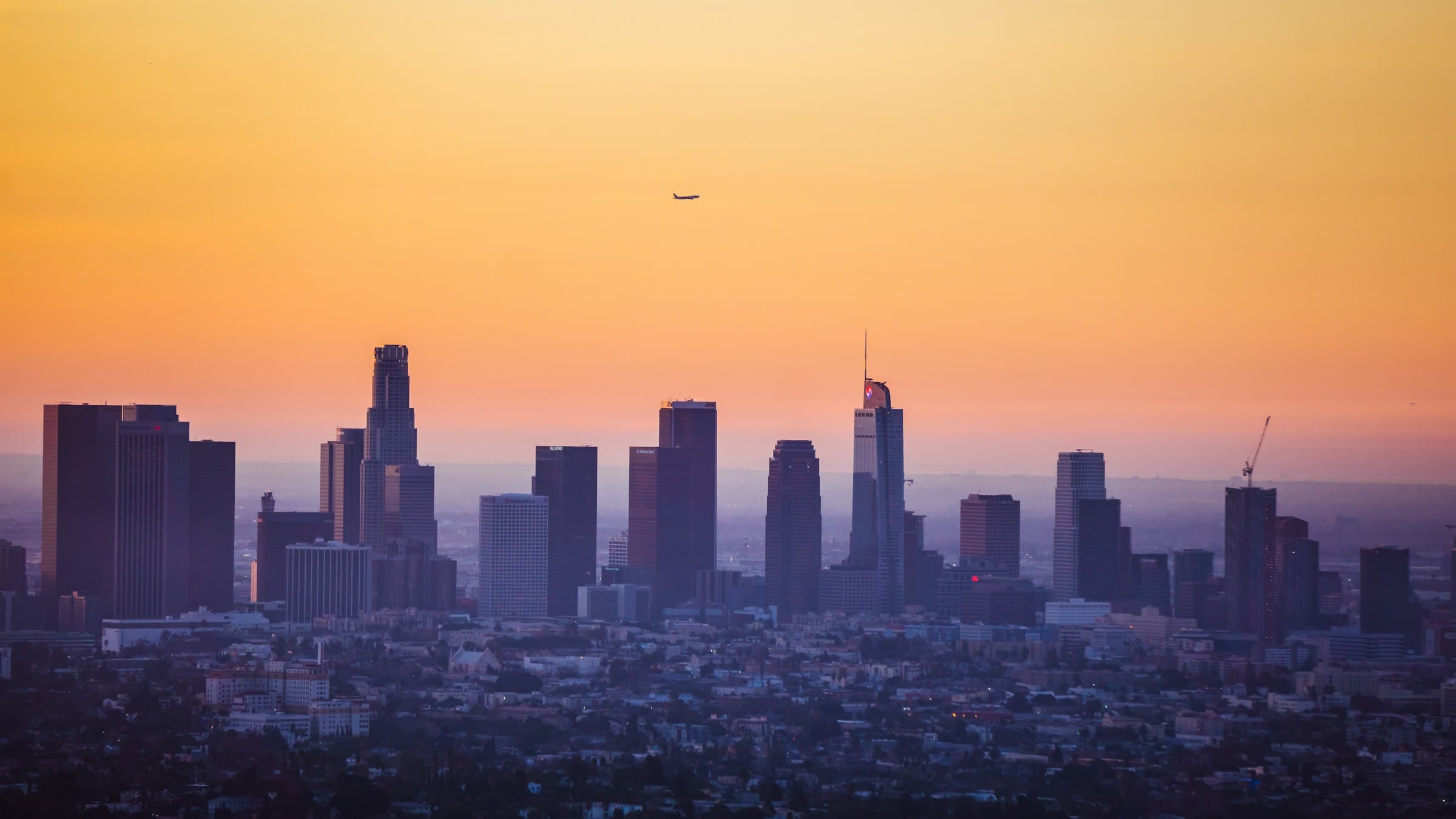 A hazy skyline at sunset with a plane overhead