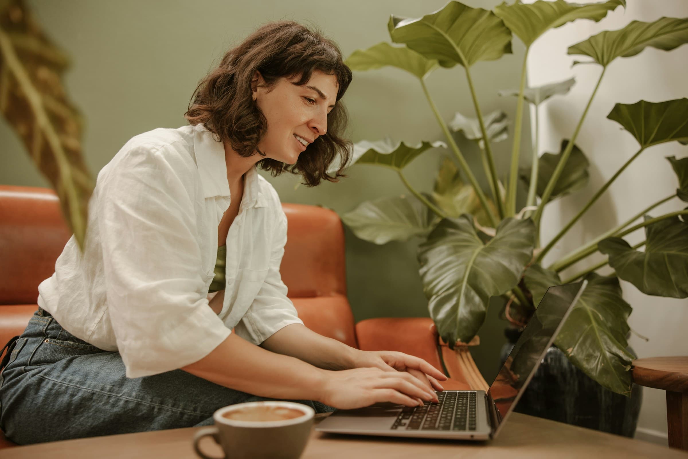 A woman on a sofa with a laptop beside plants