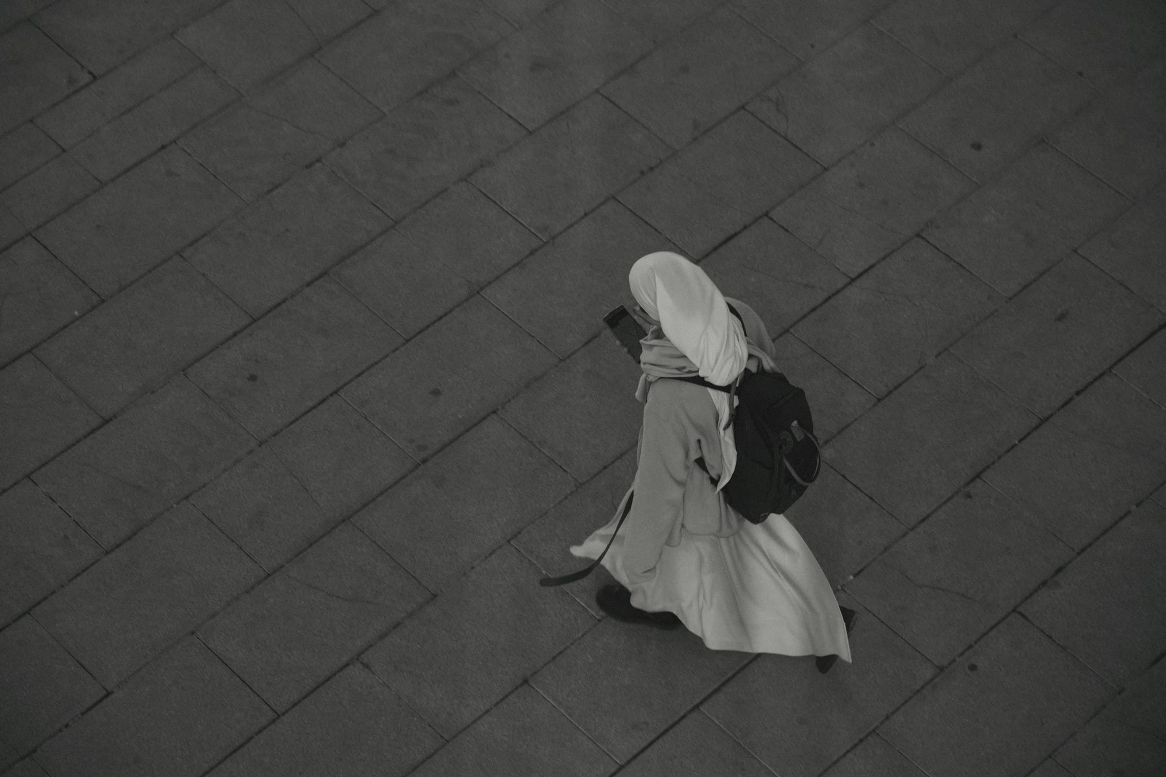 A person in white walking across grey paving, seen from above